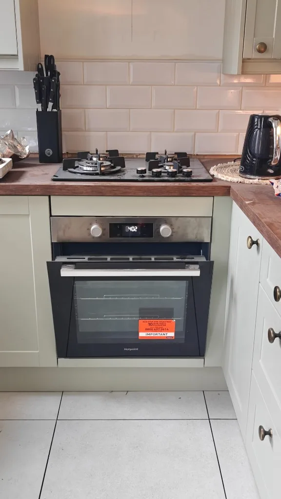 Black glass gas hob installed above Hotpoint built-in oven with sage green cabinets