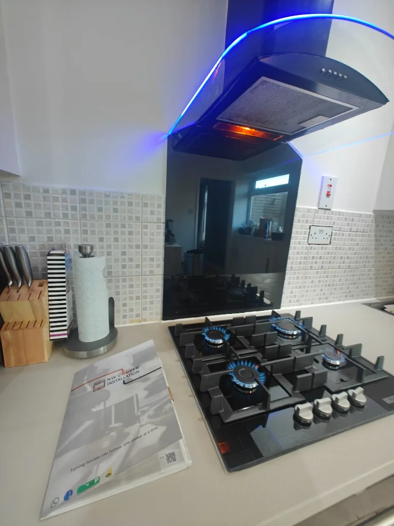 Black glass gas hob with blue burner flames, glass splashback and curved extractor hood after installation